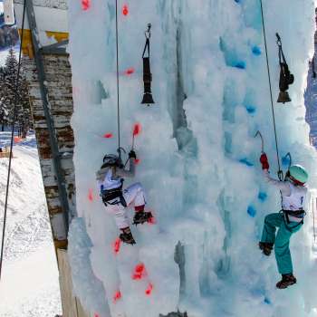 Zwei Kinder beim Eisklettern am gefrorenen Kletterturm in Malbun mit Eispickeln und Helmen