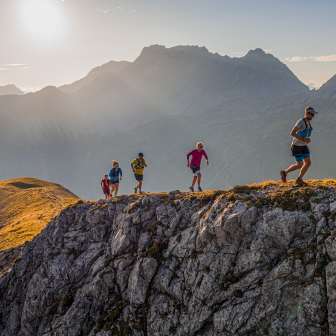 Gruppe von Trailrunnern auf einem felsigen Grat in den Bergen von Liechtenstein bei Morgensonne und beeindruckender Alpenkulisse