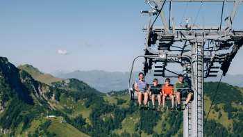 Eine Familie fährt mit der Sesselbahn Sareis über eine grüne Berglandschaft