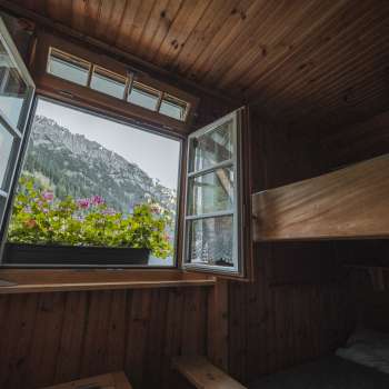 Fensterblick aus dem Schlafraum: Blick aus einem einfachen Schlafraum mit Stockbett der Gafadurahütte auf die Berglandschaft.