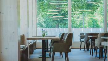 Helles, modernes Restaurant mit Holzverkleidung, bequemen Sitzmöbeln und großflächigen Fenstern mit Blick ins Grüne
