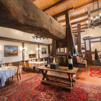 Rustikaler Speisesaal mit historischem Holzbalken, Kamin und gedeckten Tischen im Restaurant Torkel.