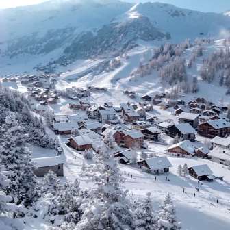 Verschneite Häuser und Skipisten im alpinen Winterdorf Malbun, eingebettet in eine traumhafte Berglandschaft.