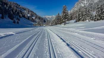 Frisch gespurte Langlaufloipe in Steg mit Panoramablick auf die verschneite Alpenlandschaft