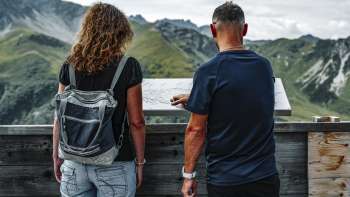 Paar sieht sich die Bergtafel auf der Terrasse des Berggasthauses Sareis an