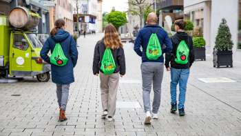 Vier junge Menschen mit grünen Rucksäcken spazieren durch die Fußgängerzone von Vaduz – unterwegs auf dem FoodTrail Vaduz
