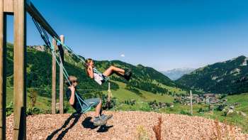 Zwei Kinder schaukeln mit der Aussicht auf Malbun