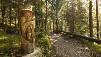 Holzfigur mit Laterne am WalserSagenWeg im mystischen Waldlicht