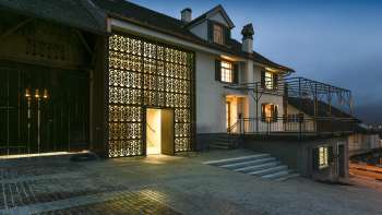 Modern beleuchtetes Kulturhaus Rössle in Mauren bei Abenddämmerung, mit Glasfassade, historischem Gebäudeanbau und gepflastertem Vorplatz.