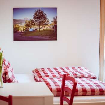 Gemütliches Doppelzimmer im Gästehaus beim Camping Mittagsspitze mit rot-weiß karierter Bettwäsche und Dekoration.