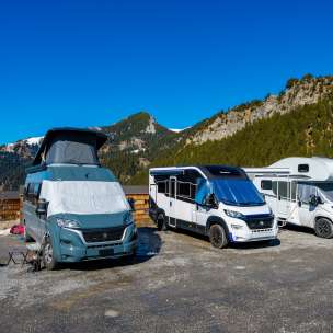 Mehrere Camper und Wohnmobile auf einem Stellplatz in den Bergen von Liechtenstein bei strahlend blauem Himmel