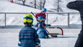 Familie beim Schlittschuhlaufen in Malbun, Kind sitzt auf einer Eislaufhilfe in Tierform.