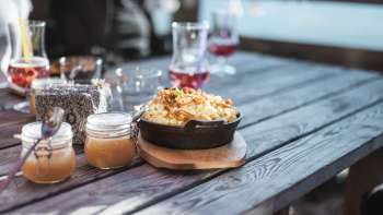 Regionale Spezialität «Käsknöpfle» mit Apfelmus auf einem Holztisch vor alpiner Kulisse