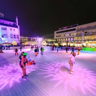 Menschen beim Eislaufen auf der beleuchteten Eisbahn von Vaduz on Ice im Stadtzentrum von Vaduz am Abend