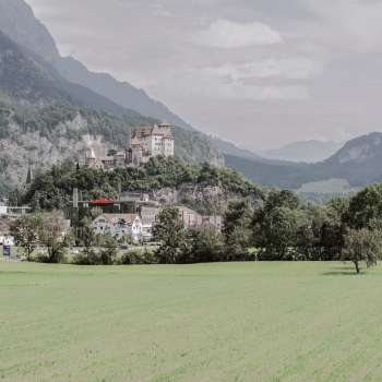 Majestätische Aussicht auf Burg Gutenberg in Balzers, umgeben von grünen Feldern und den beeindruckenden Alpen.