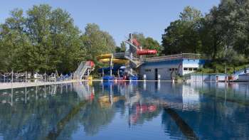 Blick auf das große Schwimmbecken mit bunter Rutschenlandschaft im Schwimmbad Mühleholz in Liechtenstein.