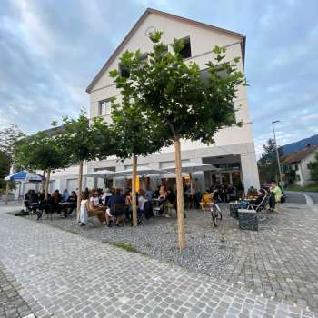 Belebte Terrasse des St. Martins Pub am Platz mit schattenspendenden Bäumen und Gästen an Tischen.
