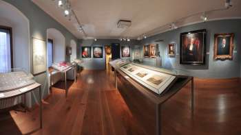 Panoramablick in einen Ausstellungsraum des Landesmuseums mit historischen Gemälden und Schaukästen.