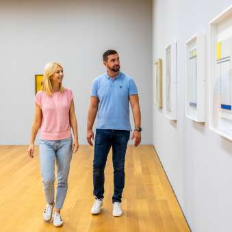 Moderne Kunst in Vaduz entdecken – ein Spaziergang durch das Kunstmuseum Ein Paar schlendert durch das Kunstmuseum Liechtenstein in Vaduz und betrachtet zeitgenössische Kunstwerke an der Wand.