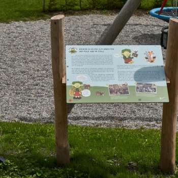 Zwei Kinder betrachten gemeinsam eine Erlebnisstation und lernen auf dem interaktiven Naturpfad „Wurz und Zirp auf Zeitreise“ über Tiere und Pflanzen in Liechtenstein.