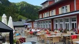 Sonnige Terrasse des Restaurants mit gedeckten Tischen, Sonnenschirmen und Alpenblick.