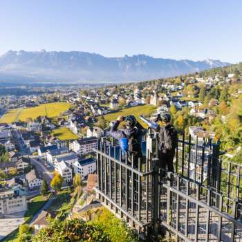 Wanderer am Geländer des Aussichtspunktes Känzile mit Panoramaausblick auf Vaduz und die umliegenden Berge.