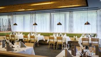 Ein einladender Essbereich mit runden Tischen und weichen grünen Stühlen, in einem modernen, natürlichen Stil eingerichtet.