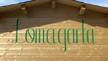Ansicht auf das grüne Lömagarta-Logo, das stilvoll auf der Holzfassade des gemütlichen Biergartens prangt.
