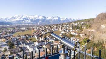 Fernrohr am Schlossweg-Aussichtspunkt Känzile mit Blick auf Vaduz und das verschneite Alpenpanorama im Hintergrund.