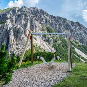 Hängeschaukel auf dem Schaukelpfad Malbun mit Blick auf steile Felswände und alpine Landschaft in Liechtenstein