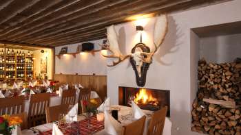 Gemütliches Restaurantambiente mit rustikalen Holzbalken, weißen Tischdecken und prasselndem Kamin. Gemütliches Restaurantambiente mit rustikalen Holzbalken, weißen Tischdecken und prasselndem Kamin.