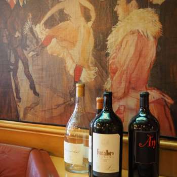Drei Weinflaschen vor einem kunstvollen Wandgemälde in der Brasserie Burg – mediterrane Eleganz trifft Kunstflair.