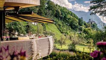 Sonnige Terrasse mit blühenden Blumen und elegant gedeckten Tischen mit Blick ins Tal