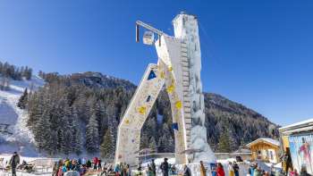 Eisturm Malbun bei blauem Himmel, umgeben von schneebedeckten Bäumen und Skifahrern