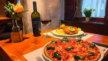 Nahaufnahme einer Pizza mit Tomaten, Käse und Basilikum auf einem Holztisch, im Hintergrund ein Glas Rotwein