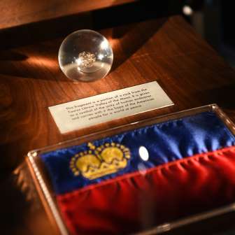 Ausstellungsstück in der Schatzkammer Liechtenstein: Liechtensteiner Flagge mit goldener Krone und gläserne Kugel mit historischem Fundstück
