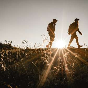 Zwei Wanderer in Liechtenstein bei Sonnenuntergang, Silhouette auf einem Bergpfad mit Naturwiese im Vordergrund