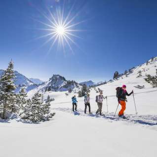 Gruppe beim Schneeschuhwandern durch die verschneite Landschaft am Schönberg bei Malbun unter strahlender Wintersonne.