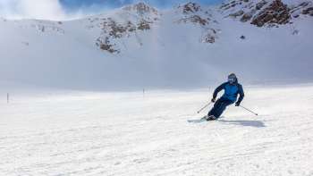 Skifahrer auf breiter Skipiste in Malbun, Liechtenstein, umgeben von verschneiten Alpenhängen und strahlend blauem Himmel