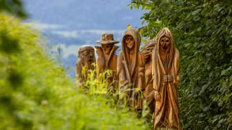 Detailansicht geschnitzter Holzfiguren in mystischer Darstellung am Walser Sagenweg in Triesenberg, umgeben von grüner Natur