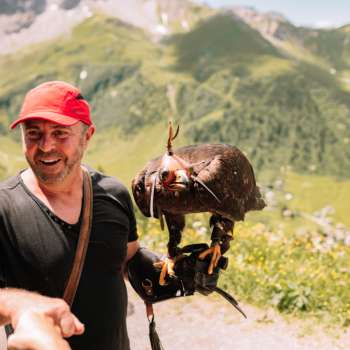 Falkner mit roter Kappe präsentiert einen majestätischen Adler in alpiner Landschaft.