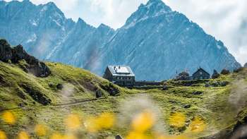 Aussicht auf die Pfälzerhütte, Sie liegt auf einer grünen Alpe vor steilen Felswänden in den Liechtensteiner Alpen.