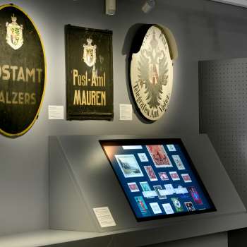 Museumsraum mit alten Postschildern und einem digitalen Display zur Geschichte der Post in Liechtenstein.