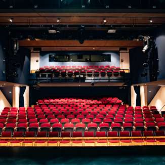 Blick von der Bühne auf rote Sitzreihen und Lichttechnik im modernen Zuschauerraum des TAK Theater Liechtenstein