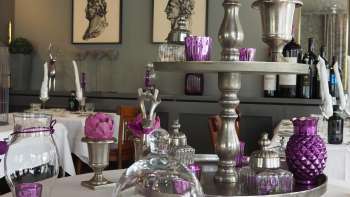 Tischdekoration mit lilafarbenen Blumen auf weisser Tischdecke