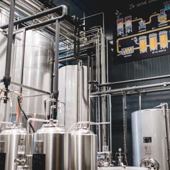 Blick in den Technikraum der Brauerei mit komplexem Leitungssystem und modernen Edelstahltanks.