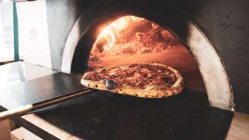 Pizza im Holzofen mit goldbraunem Rand und knuspriger Kruste