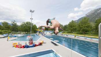 unge springt mit Salto vom 1-Meter-Brett ins Becken des Schwimmbads Mühleholz – Sommerfreude pur.