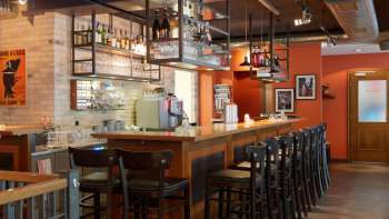 oderne Bar im New Castle Vaduz mit langer Holztresen, hohen Stühlen und hängenden Glasregalen in warmem Ambiente.