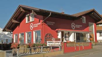 Rotes Gebäude des Restaurant Kainer mit Holzbalkon und einladendem Aussenbereich Rotes Gebäude des Restaurant Kainer mit Holzbalkon und einladendem Aussenbereich